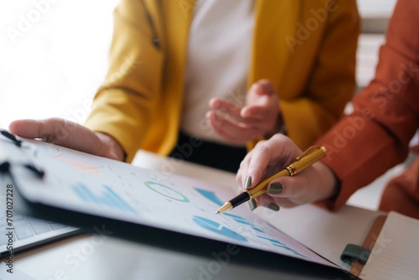 Fototapeta Meeting of businesswomen pointing at graph. Group of businesspeople discussing together at a meeting.