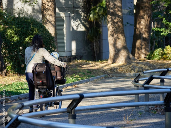 Fototapeta 冬の公園でママチャリを押して子供と保育園に行く若い母親の姿