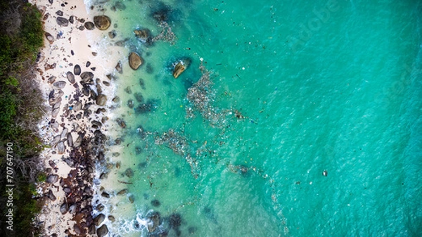 Fototapeta Aerial view of a tropical beach with crystal-clear water, sandy shore, and scattered rocks, depicting a serene vacation destination