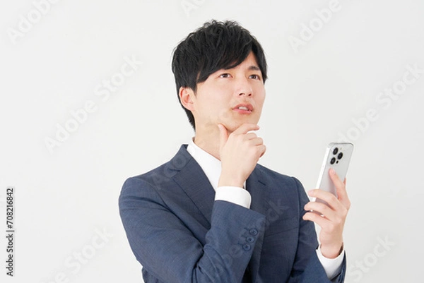 Fototapeta スマートフォンを持って考えるビジネスマン　白背景