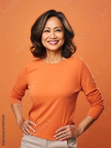 Fototapeta Middle-aged filipino woman smiling and posing confidently on a orange background. Businesswoman studio portrait 