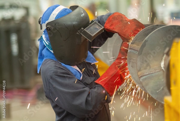 Fototapeta Worker using an angle grinder, making a screw conveyor