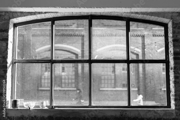 Fototapeta View through an old factory window frame in an industrial setting with cyclists out of focus in the background.