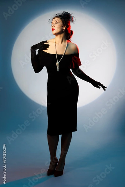 Fototapeta An elegant young woman in retro-style clothes poses in full height.