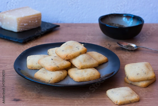 Fototapeta Cheese crackers on a dark plate on wooden table