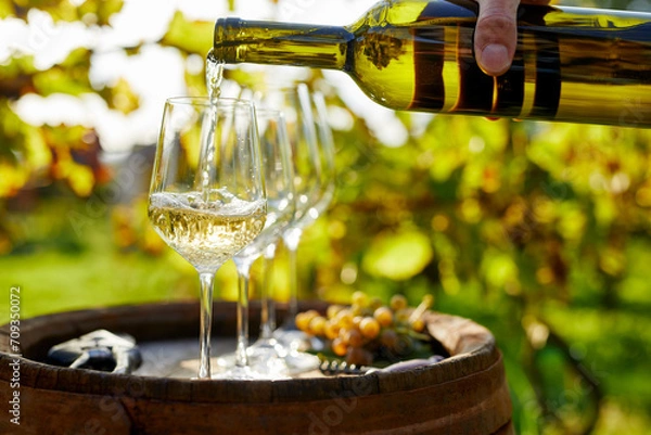 Obraz A man pours white wine into glasses on a wooden barrel