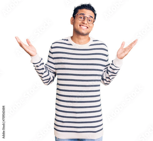 Obraz Hispanic handsome young man wearing casual clothes and glasses celebrating crazy and amazed for success with arms raised and open eyes screaming excited. winner concept