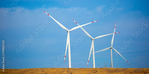 Fototapeta Fleet of power generators in motion. The blades of the wind farm rotate against the sky. The concept of extracting electricity from renewable sources. Wind turbine to generate electricity.