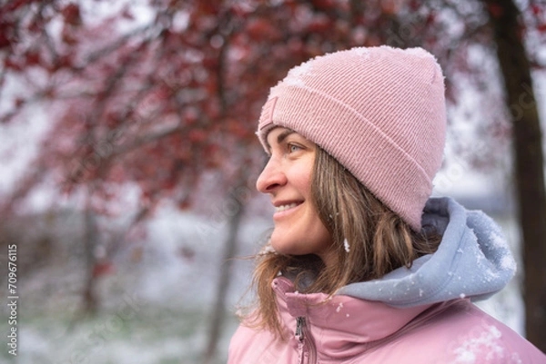 Fototapeta Winter Elegance: Portrait of a Beautiful Girl in a Snowy European Village. Winter lifestyle portrait of cheerful pretty girl. Smiling and having fun in the snow park. Snowflakes falling down
