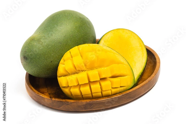 Fototapeta Sliced half cut into cubes and whole fresh organic green mango delicious fruit side view in a wooden plate isolated on white background clipping path