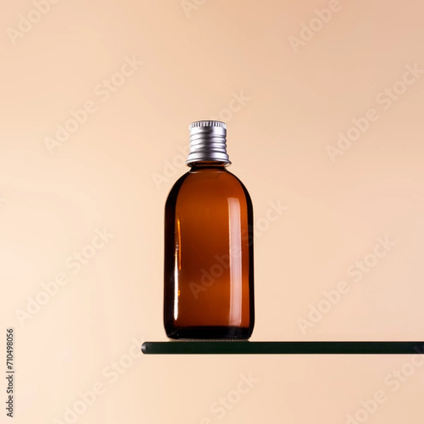 Fototapeta Brown glass bottle with silver cap mock ap on a beige background. Anti aging concept, hyaluronic acid and collagen with peptides .