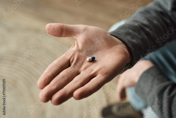 Fototapeta cropped view of man holding blue and white capsule, close up photo of medication in male hand