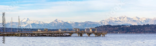 Fototapeta A fishing pier extends out into the ocean with a backdrop of mountains and a cloudy sky