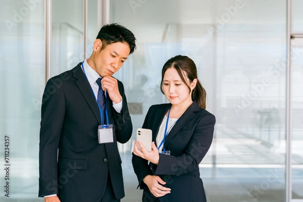 Obraz スマホを見ながら考え事をするビジネスマンとビジネスウーマン（ストレス・悩む・困る・問題）
