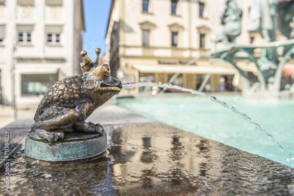 Obraz Brunnenskulptur Froschkönig mit Wasserstrahl vor Häuserkulisse am Marktbrunnen in Ehingen an der Donau