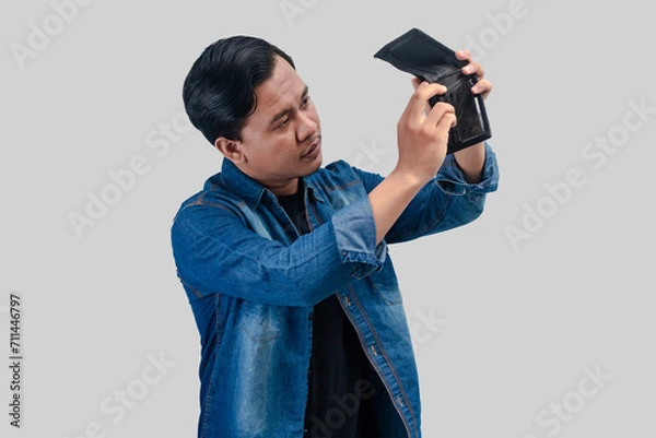 Fototapeta Young Asian man showing sad face expression while holding his empty wallet