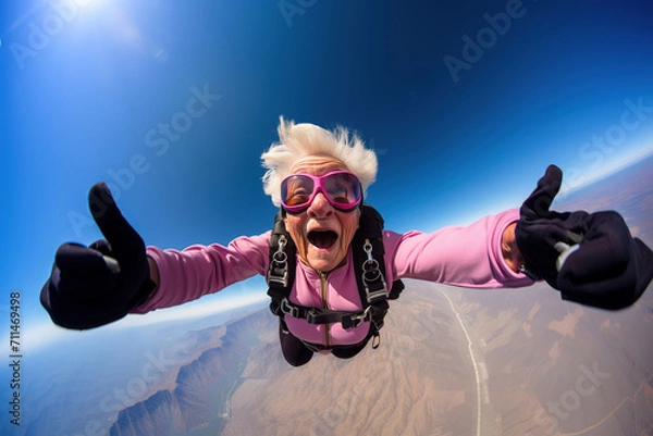 Fototapeta Cheerful old granny trying skydiving in the sky and showing thumbs up.