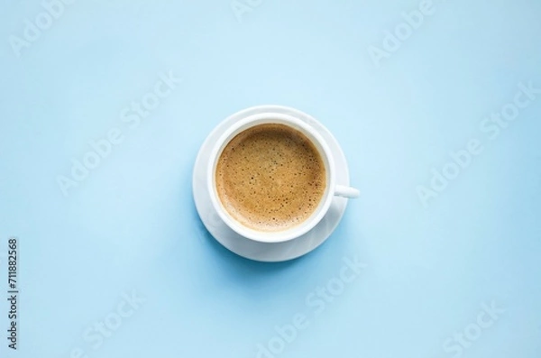 Obraz On a blue background there is a white cup with hot, aromatic, delicious cappuccino coffee. Flat lay, top view, close-up. Concept coffee break, hot drinks. Space for copying text.


