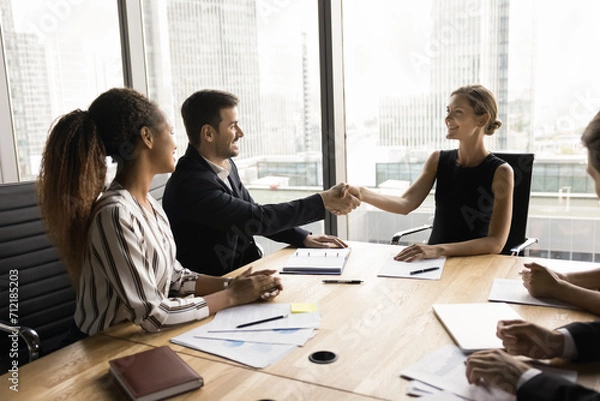 Obraz Successful young female business leader holding meeting with partners, investors, multiethnic team of colleagues, shaking hands with male manager, discussing agreement, corporate success