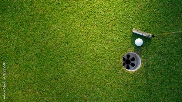 Fototapeta Top view of a golf ball with putter on green course at hole.