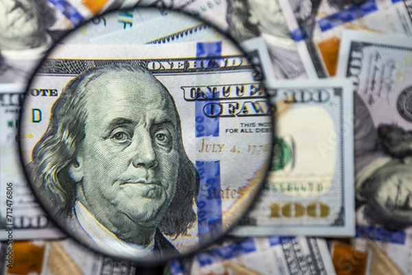 Fototapeta 100 american dollar notes background with Benjamin Franklin face portrait magnified with a magnifying glass. Monetary wallpaper.