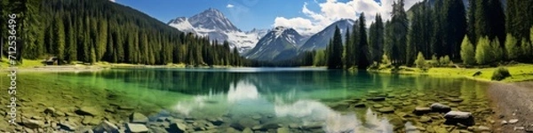 Fototapeta A panoramic shot of a crystal-clear glacial lake,  surrounded by snow-capped peaks and lush evergreen forests