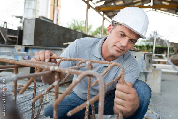 Obraz man in overalls works with metal structure outdoors
