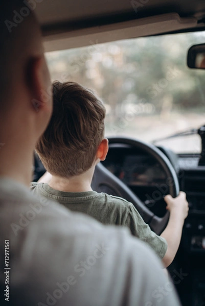 Obraz Dad teaches his son to drive a car view from the back