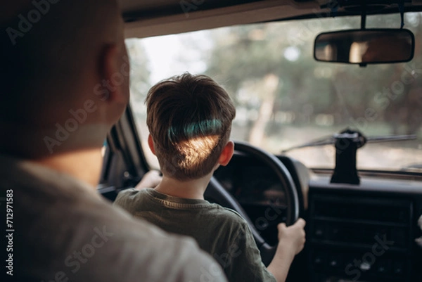 Obraz Dad teaches his son to drive a car view from the back