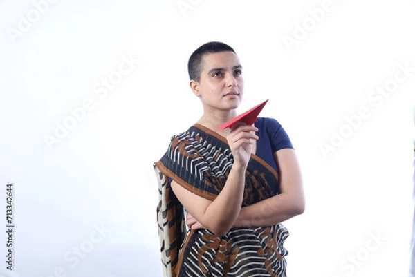 Obraz Beautiful Indian widow woman in saree dreaming of going for an air travel. She is holding an paper plane in hand. Various rural India expressions. Woman is bald and has a trimmed hair on head.