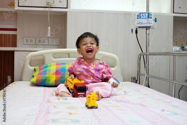 Fototapeta 2-year-old baby in patient uniform Lying laughing, smiling in a hospital bed.