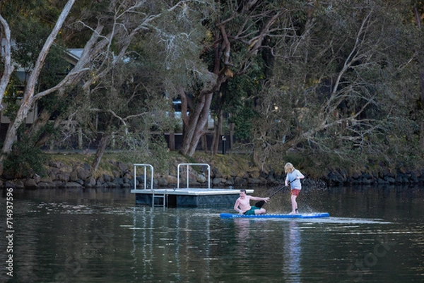Fototapeta Kids sharing stand up paddle board on small lake with pontoon