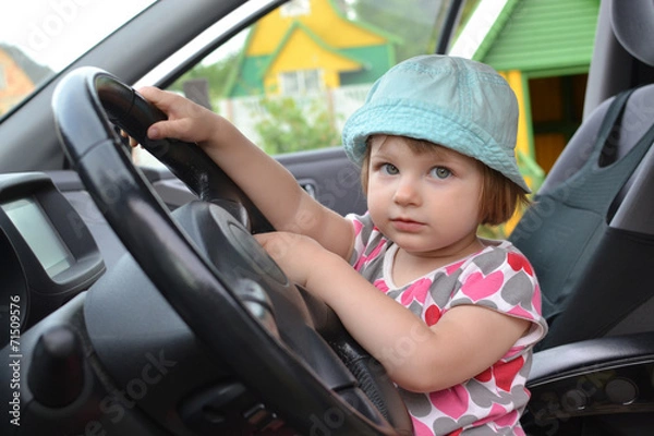 Fototapeta Cute little girl is sitting behind the wheel of a  car