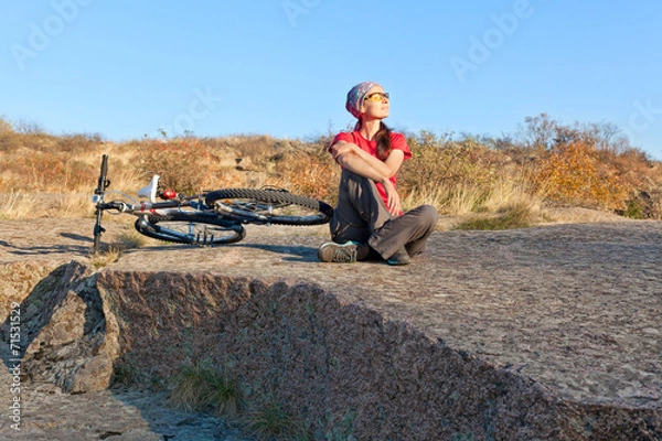 Obraz Woman sitting on a stone next to mountain bike relaxing and enj