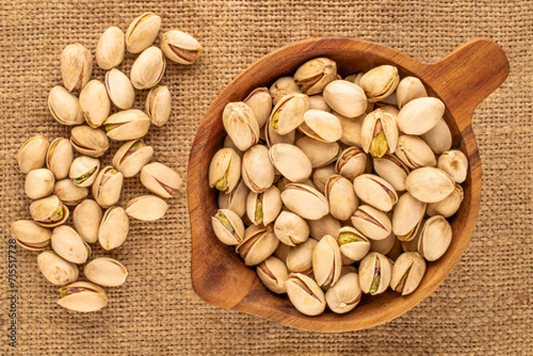Obraz Small amount of roasted pistachios with wooden cup on jute cloth, macro, top view.