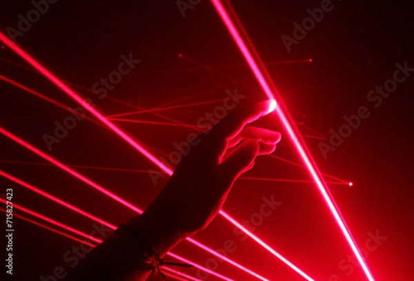 Fototapeta close-up hand touching the red line of a laser beam in a dark room.