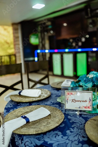 Fototapeta a round table decorated with a blue tablecloth, plate holder and a flower arrangement with a glass vase