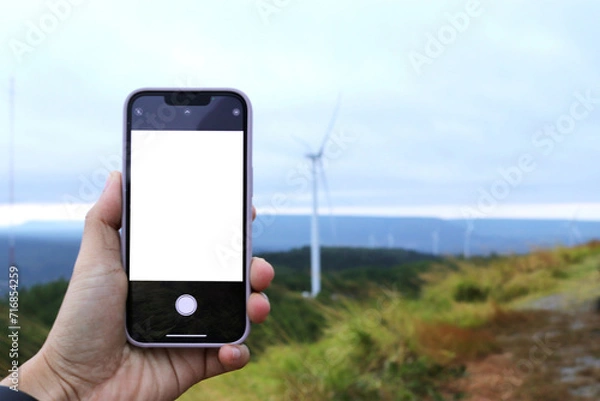Obraz Woman holding mobile phone with blank screen while, With of windmill landscape view. Clean energy concept, wind power