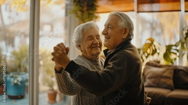 Fototapeta Happy Senior Couple Dancing Having Fun At Home On Weekend. Husband And Wife Enjoying Retired Life Having Date In Living Room. Retirement Hobby And Leisure For Mature Spouses Concept