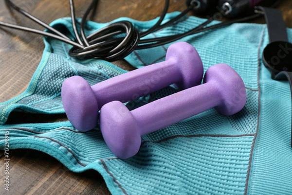 Fototapeta Dumbbells and sportswear on wooden background
