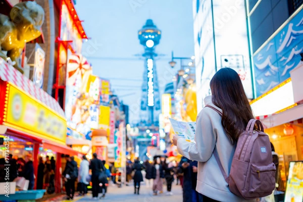 Obraz Asian female tourist Traveling and having fun. And she was taking photo with a cell phone camera at Night street with many restaurant around Tsutenkaku Tower in Shinsekai district of Osaka, Japan.