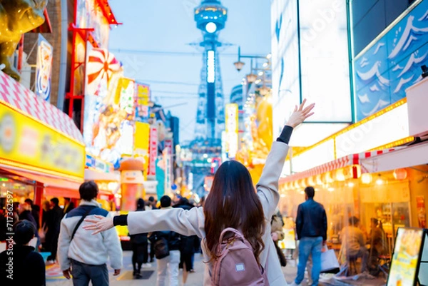 Obraz Asian female tourist Traveling and having fun. And she was taking photo with a cell phone camera at Night street with many restaurant around Tsutenkaku Tower in Shinsekai district of Osaka, Japan.