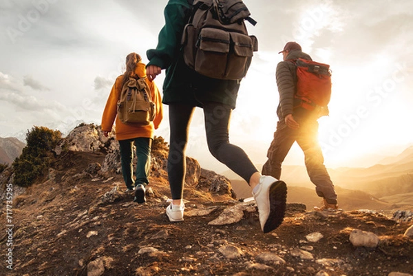 Obraz Three young hikers with small backpacks walks in sunset mountains. Close up photo of tourist legs in sunset light