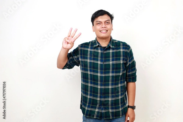 Fototapeta Happy young adult Indonesian man standing while showing three fingers. Isolated on white