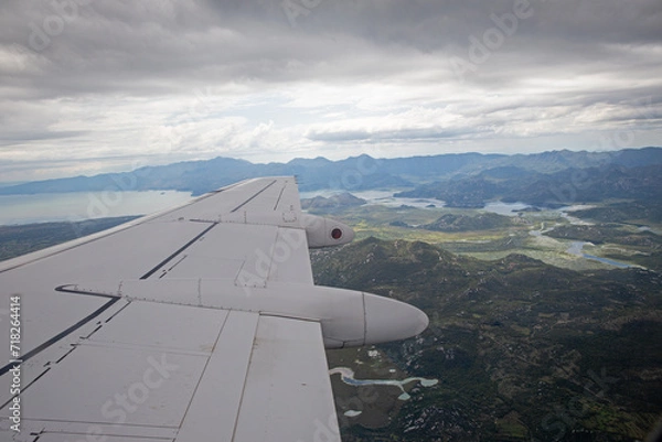 Fototapeta Aerial view by the airplane wing while flying above the beautiful Montenegro landscape before landing at the Podgorica airport, wide angle shot