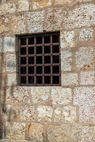 Fototapeta Window with rusty iron bars, stone wall