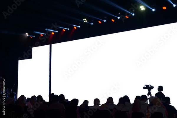 Obraz Audience in silhouette watching a presentation with a large blank projection screen, event and conference concept.