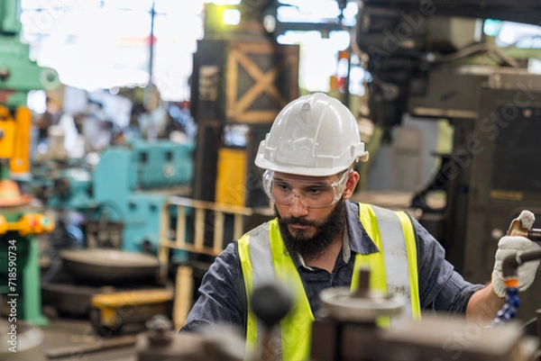 Fototapeta The technician is working in a steel factory. Worker wearing protective gear operating heavy machinery inside the steel factory.