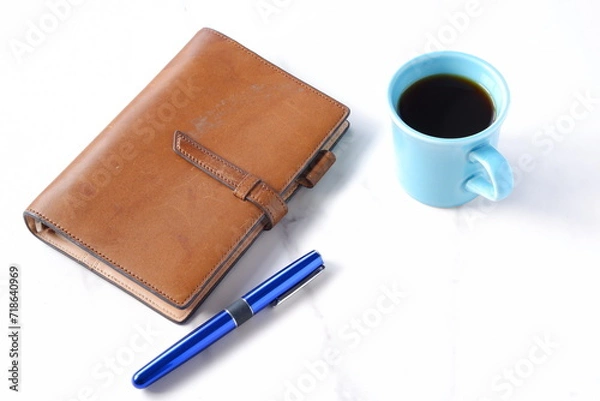 Fototapeta コーヒーを飲みながら、茶色の革のシステム手帳でデスクワークをしているイメージ
