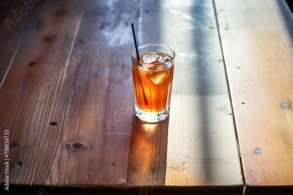 Fototapeta backlit iced tea glass casting a long shadow on wood